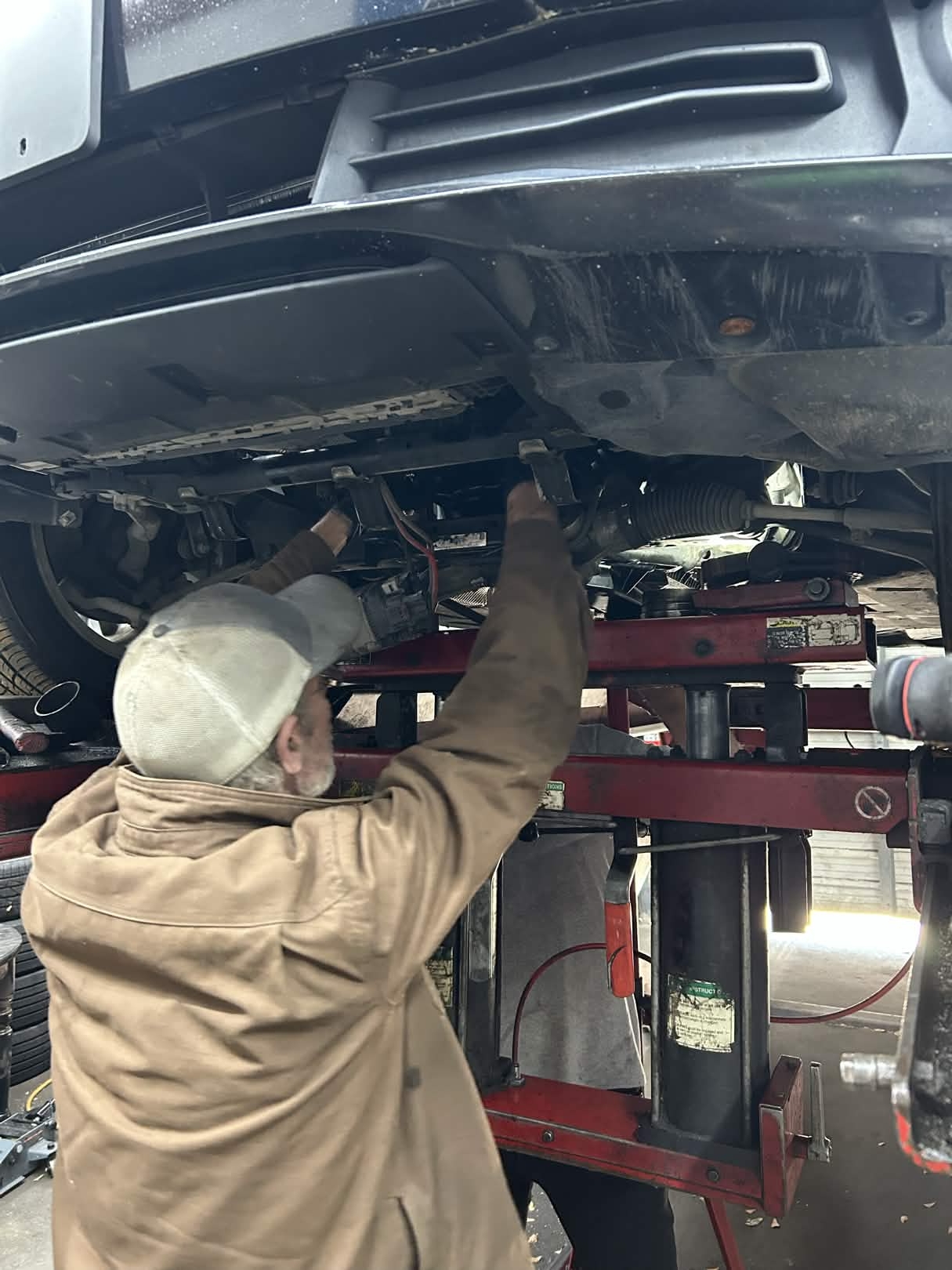 Technician inspecting steering and suspension components on a vehicle raised on the lift